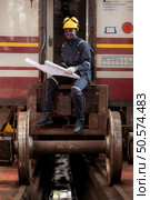 Railway technician in uniform and helmet inspect the train wheels removed from the locomotives in the train workshop. Стоковое фото, агентство Ingram Publishing / Фотобанк Лори