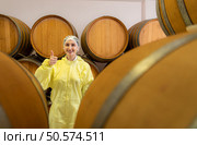 Smiling female winemaker in yellow uniform standing in cellar of winery. Стоковое фото, агентство Ingram Publishing / Фотобанк Лори