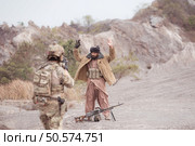 A Taliban soldier stands with a machine gun, Raise hands in surrender to the allied soldiers, In the desert mountain terrain battlefield. Стоковое фото, агентство Ingram Publishing / Фотобанк Лори