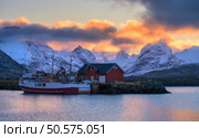 Red fishing boats on the sea, reflection in water, snowy mountains, colorful purple sky with pink clouds at sunset. Lofoten islands, Norway. Winter landscape with boats in harbor, fjord, rorbu at dusk. Стоковое фото, агентство Ingram Publishing / Фотобанк Лори