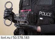 Police officer holding handcuffs and supermarket trolley in concept of shoplifting. Стоковое фото, агентство Ingram Publishing / Фотобанк Лори