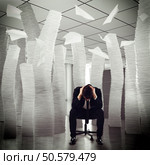 Desperate businessman sitting among piles of papers. Endless debts. Стоковое фото, агентство Ingram Publishing / Фотобанк Лори
