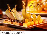 Closeup image of canapes with cheese, grapes, apple slices on a plate at wooden table background. Стоковое фото, агентство Ingram Publishing / Фотобанк Лори