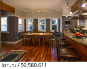 Dining room table and chairs and kitchen breakfast bar with wood floors, granite countertops, accent lighting and view windows in contemporary upscale home interior. Стоковое фото, агентство Ingram Publishing / Фотобанк Лори