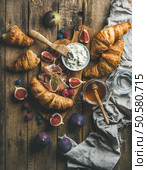 Breakfast with freshly baked croissants, ricotta cheese, figs, fresh berries, prosciutto di Parma and honey in glass jar over rustic wooden background, top view, vertical composition. Breakfast with croissants, honey, ricotta cheese, fresh berries and prosciutto. Стоковое фото, агентство Ingram Publishing / Фотобанк Лори