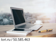 Sideview of wooden table with laptop, coffee cup, phone and pen on blurry city background. Стоковое фото, агентство Ingram Publishing / Фотобанк Лори