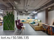Interior in a loft style with a big zone with wooden benches and seats. Benches are decorated with grass, plants and bricks. On the right there is a gray table with orange legs and two chairs. In the center there are two purple armchairs with small round table with a glass and a book. On the left there is a gray ornamental stand decorated with grass. At the top there are communications, lamps and speakers. Place for coworking.. Coworking in loft style. Стоковое фото, агентство Ingram Publishing / Фотобанк Лори