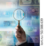 Businessman holding magnifying glass up to world currencies. 24316771. Стоковое фото, агентство Ingram Publishing / Фотобанк Лори