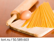 Wooden chopping board with egg and uncooked pasta piled up, rolling pin on desk next to it.. Wooden chopping board with egg and uncooked pasta piled up, rolling pin on desk next to it. Стоковое фото, агентство Ingram Publishing / Фотобанк Лори