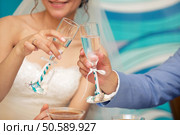 glasses of the groom and bride in hands with a blue tape. Bride and groom with glasses of champagne. Стоковое фото, агентство Ingram Publishing / Фотобанк Лори