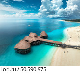Aerial view of bungalow, white sandy beach, ocean on summer sunny day. Restaurant on the sea. Top drone view of wooden hotel, azure water, palms, sky with clouds. Luxury resort in Kendwa, Zanzibar. Стоковое фото, агентство Ingram Publishing / Фотобанк Лори