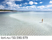 Aerial view of alone young woman on the sandbank in ocean, white sand, blue sea during low tide on sunny summer day in Zanzibar island. Top view of girl, sand spit, bay, clear water, sky with clouds. Стоковое фото, агентство Ingram Publishing / Фотобанк Лори