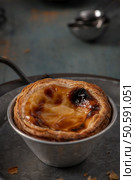 A delectable pastel de nata with a perfectly flaky crust and a creamy, caramelized custard filling, served in a traditional metal tin. Стоковое фото, агентство Ingram Publishing / Фотобанк Лори