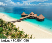 Aerial view of bungalow, white sandy beach, ocean on summer sunny day. Restaurant on the sea. Top drone view of wooden hotel, azure water, green palms. Luxury resort in Kendwa, Zanzibar. Tropical. Стоковое фото, агентство Ingram Publishing / Фотобанк Лори