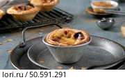 A Portuguese custard tart in a metal tin sits on a round tray with others on a rack cinnamon and measuring spoons in the background. Стоковое фото, агентство Ingram Publishing / Фотобанк Лори