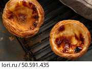 Two golden-brown, freshly baked Portuguese custard tarts with flaky, crispy crusts sit invitingly on a black wire rack, ready to be enjoyed. Стоковое фото, агентство Ingram Publishing / Фотобанк Лори