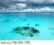 Aerial view of colorful boats and yachts in clear water on sunny summer day. Mnemba island, Zanzibar. Top view of sandbank in low tide, blue sea, swimming people, yachts, dramatic sky with clouds. Стоковое фото, агентство Ingram Publishing / Фотобанк Лори