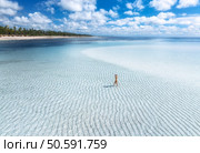Aerial view of alone young woman on the sandbank in ocean, white sand, blue sea during low tide on sunny summer day in Zanzibar island. Top view of girl, sand spit, bay, clear water, sky with clouds. Стоковое фото, агентство Ingram Publishing / Фотобанк Лори