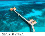 Aerial view of bungalow, jetty, sandy beach, ocean on summer sunny day. Restaurant on the blue sea. Top drone view of wooden hotel, azure water. Luxury resort in Zanzibar. Tropical background. Travel. Стоковое фото, агентство Ingram Publishing / Фотобанк Лори