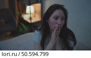 A young adult woman sits on a couch in the middle of the night, nervously twirling her hair. A lamp is on in the background. Panic attacks and mental health. Стоковое видео, видеограф Денис Кебедов / Фотобанк Лори