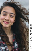 Closeup shot of pretty teenage girl with long dark curly hair wearing casual cozy plaid shirt, staying alone, thinking, dreaming, watching at camera, catching wind in her haircut. Стоковое AI-видео, аниматор Sergey Grishin / Фотобанк Лори