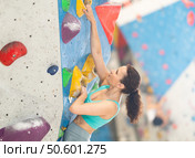 Woman in comfortable athletic clothing moving carefully on bouldering wall clinging to colorful hand and foot holds. Стоковое фото, фотограф Яков Филимонов / Фотобанк Лори