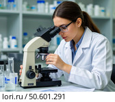 A young female doctor examines a tissue or biological fluid sample provided for analysis under a microscope. Стоковое AI-изображение, AI-художник Сергей Елизарьев / Фотобанк Лори