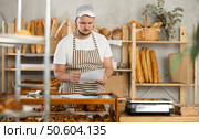 Bakery employee in apron examines documents, ponders debt restructuring. Стоковое фото, фотограф Яков Филимонов / Фотобанк Лори