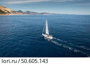 Aerial view of floating sailboat and rocky sea coast at summer sunny day. Top drone view of yacht, mountains, trees and blue water. Yachting in Sardinia, Italy. Tropical seascape with boat in ocean. Стоковое фото, агентство Ingram Publishing / Фотобанк Лори