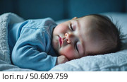 A close-up portrait of a cute, peaceful baby sleeping soundly on a blue pillow at night in a dark bedroom. Стоковое AI-видео, аниматор Sergey Grishin / Фотобанк Лори
