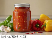 A sealed glass jar showcases delightful lecho, a chunky sauce teeming with roasted red peppers, tomatoes, and onions. The glossy container highlights vivid colors, promising a delectable, spicy experience. Стоковое AI-изображение, AI-художник Nart / Фотобанк Лори