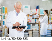 Mature male pharmacist restocking with tablet while woman apothecary working in drugstore. Стоковое фото, фотограф Татьяна Яцевич / Фотобанк Лори
