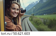 Beautiful happy young woman hangs out of train open window and make photo on vintage analog camera. Travel and explore more wanderlust concept. Female touristin. Стоковое AI-видео, аниматор Sergey Grishin / Фотобанк Лори