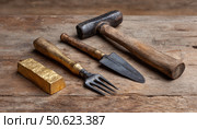 Gold ingot, hammer, pitchfork and trowel lying on wooden table. Стоковое AI-изображение, AI-художник Юрий Поздников / Фотобанк Лори