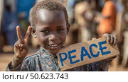 Young african child showing peace sign and holding wooden peace sign. Стоковое AI-изображение, AI-художник Юрий Поздников / Фотобанк Лори