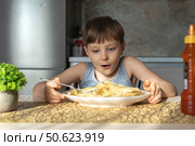 Happy boy eating tasty pasta at table in kitchen. Стоковое фото, фотограф Михаил Яковлев / Фотобанк Лори