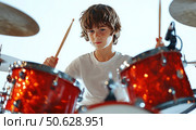 A young boy is playing drums in a red drum set. Стоковое AI-изображение, AI-художник Ярославский Максим / Фотобанк Лори