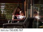 Enjoying a Sunlit Moment in a Cozy Outdoor Space With a Stylish Hanging Chair. Стоковое фото, фотограф Aleksandr Golubev / Фотобанк Лори