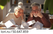 Older couple struggling with paperwork and bills at kitchen table in morning sunlight. Стоковое AI-изображение, AI-художник Сергей Толмачёв / Фотобанк Лори