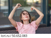 Симпатичная брюнетка поправляет волосы руками в течение дня на улице. Красивая молодая женщина сидит летом на плетеном диване возле ресторана. Томный взгляд. Стоковое фото, фотограф Роман Дорохов / Фотобанк Лори