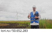 Young engineer raises his finger up and smiles at camera, thereby supporting creation of wind turbines that generate sustainable, environmentally friendly electricity. Стоковое видео, видеограф Strunov David / Фотобанк Лори