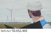 Chief engineer, wearing construction helmet, glasses, and vest, studies documentation and drawings for wind farm located in an agricultural field. Стоковое видео, видеограф Strunov David / Фотобанк Лори