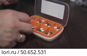 Hand placing light-yellow vitamin D capsules into a weekly pill organizer for medication management. Стоковое видео, видеограф Татьяна Степанищева / Фотобанк Лори