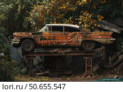 Rusty vintage car resting on a makeshift platform in a junkyard. Стоковое AI-изображение, AI-художник Иван Рябоконь / Фотобанк Лори