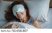 Happy millennial woman lying in bed with sleeping mask. Стоковое AI-видео, аниматор Sergey Grishin / Фотобанк Лори