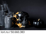 Halloween celebration. Black skull with golden roses, pumpkins, and black candles. Decor for the Day of the Dead or Halloween on a black background. Стоковое фото, фотограф Photojuli / Фотобанк Лори