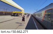 Люди прогуливаются по перрону вдоль железнодорожных вагонов. Пассажиры ходят по платформе во время остановки поезда. Современная железнодорожная станция. Россия, Ярославль, 22 мая 2025. People walking along platform along railway cars. Passengers walk on platform during train stop. Modern railway station. Russia, Yaroslavl, May 22, 2025. Редакционное видео, видеограф Ирина / Фотобанк Лори
