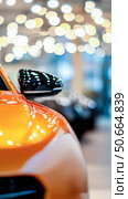 Sleek orange car's front fender and side mirror are prominently featured against blurred background of warm, shimmering bokeh lights. Perfect for automotive, luxury and technology themes. Стоковое AI-изображение, AI-художник Елена Никишина / Фотобанк Лори