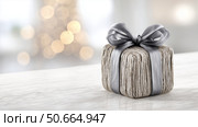 Gift wrapped in grey ribbon on marble surface with festive background lights. Стоковое AI-изображение, AI-художник Katsiaryna Repich / Фотобанк Лори
