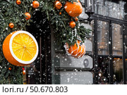 Mandarins in a string bag and Christmas tree decorations on the streets of Moscow. Happy New Year 2026. The concept of preparing decorations and ornaments for Christmas. Стоковое фото, фотограф Photojuli / Фотобанк Лори